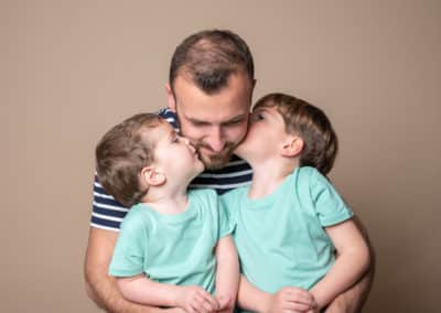 père avec ses deux enfants lui faisant un bisou habiller en bleu