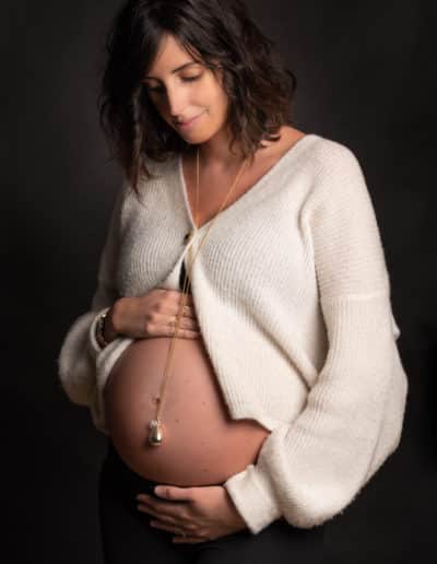 femme enceinte habillée en blanc sur fond noir en shooting photo