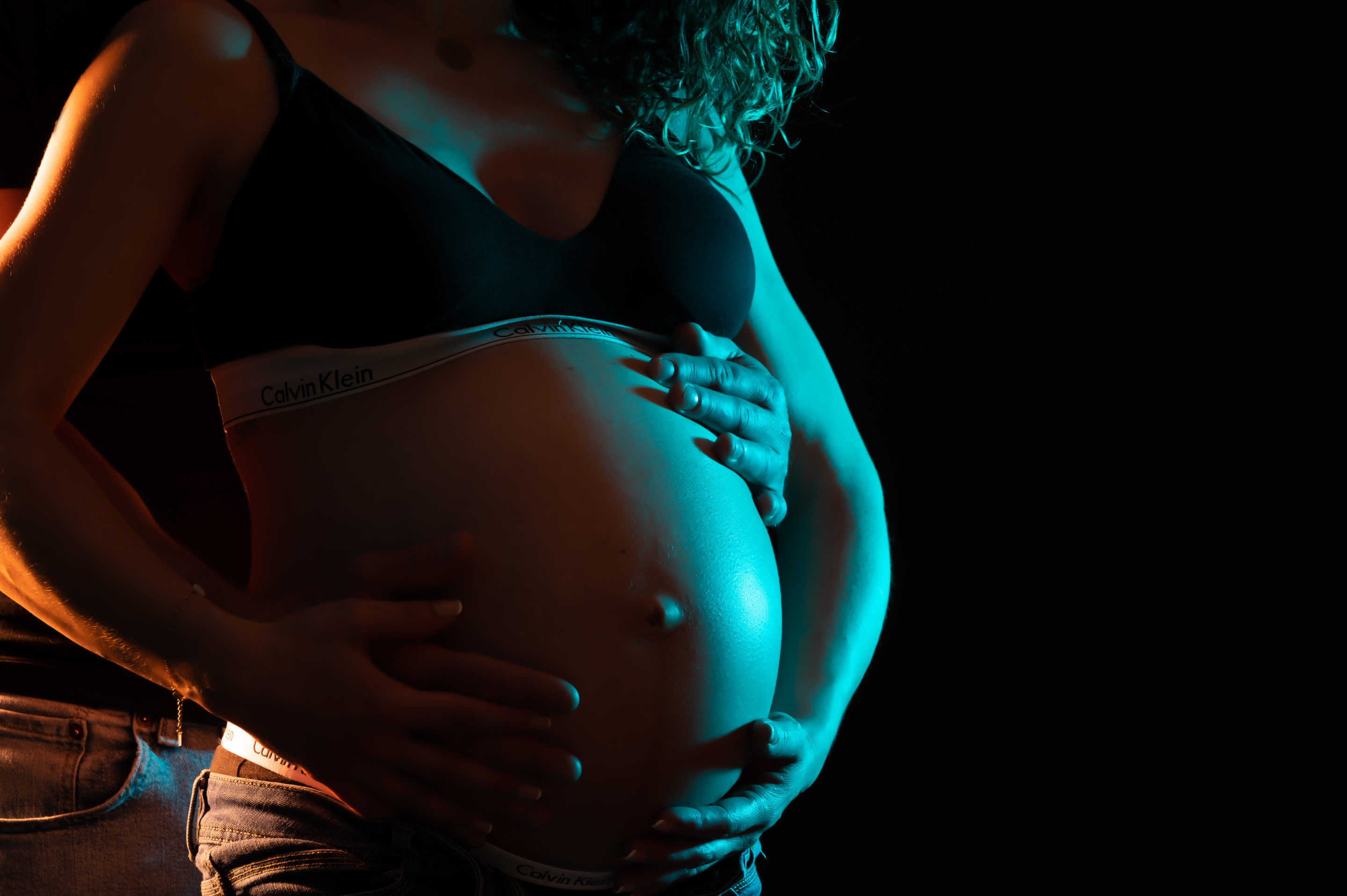 femme enceinte avec son homme lumière orange et bleu en studio photo